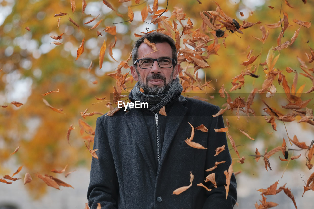 Portrait of young man standing by leaves during autumn