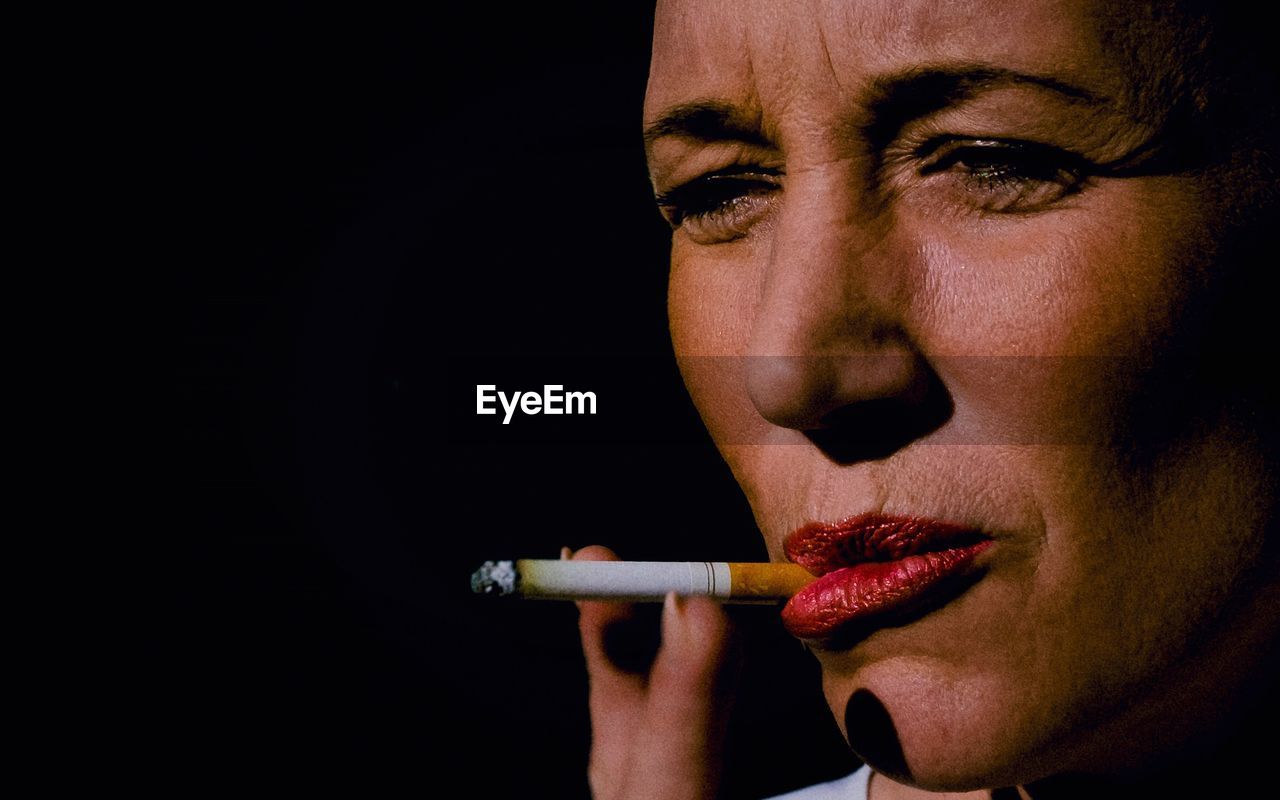 Close-up portrait of woman smoking cigarette against black background
