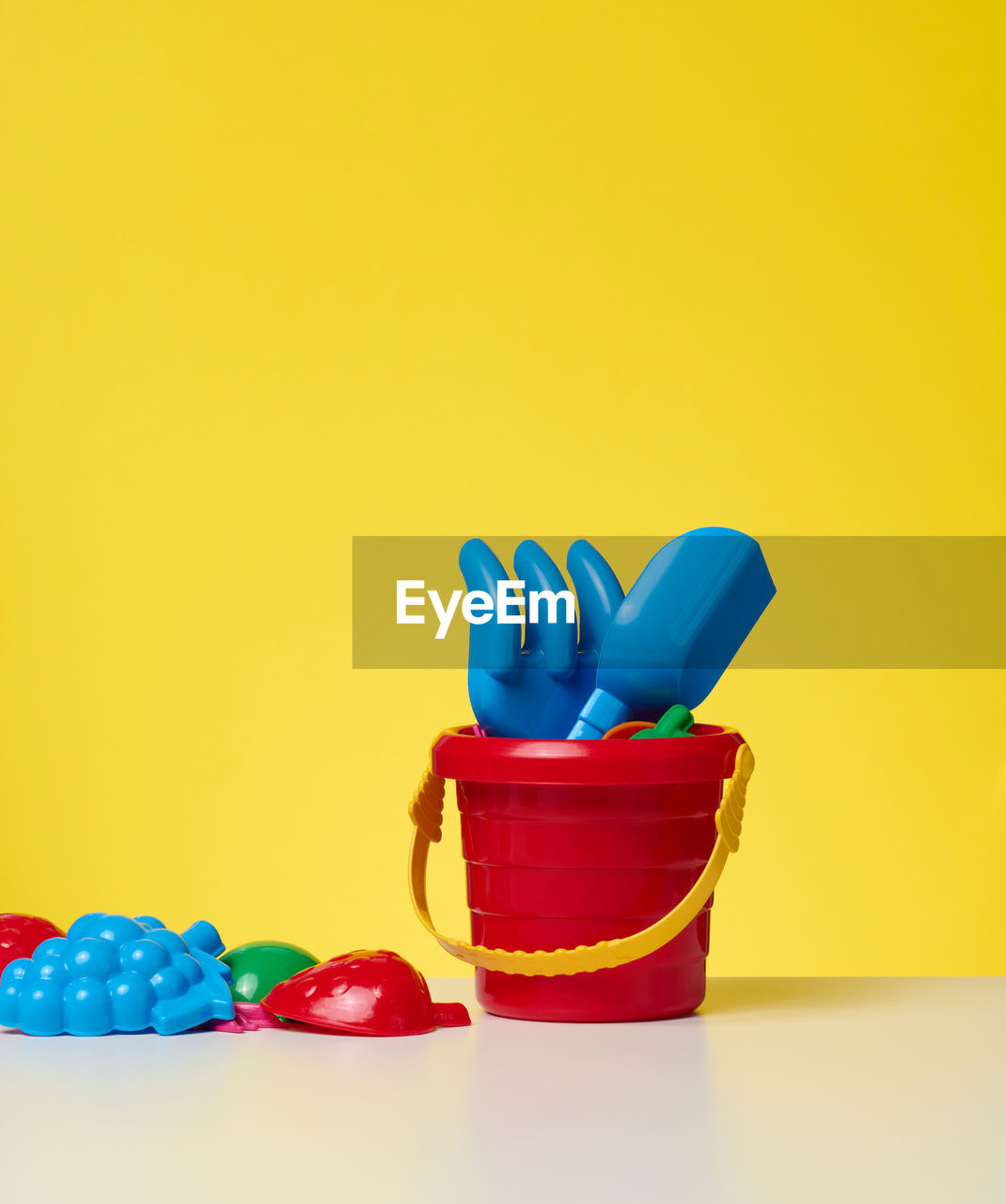 Baby red plastic bucket with shovel and toys on a yellow background. outdoor items