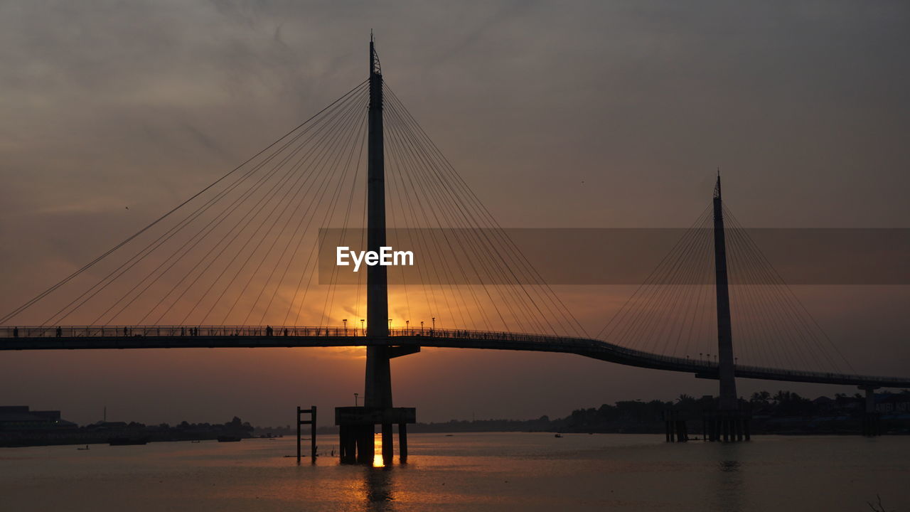 View of suspension bridge over river at sunset