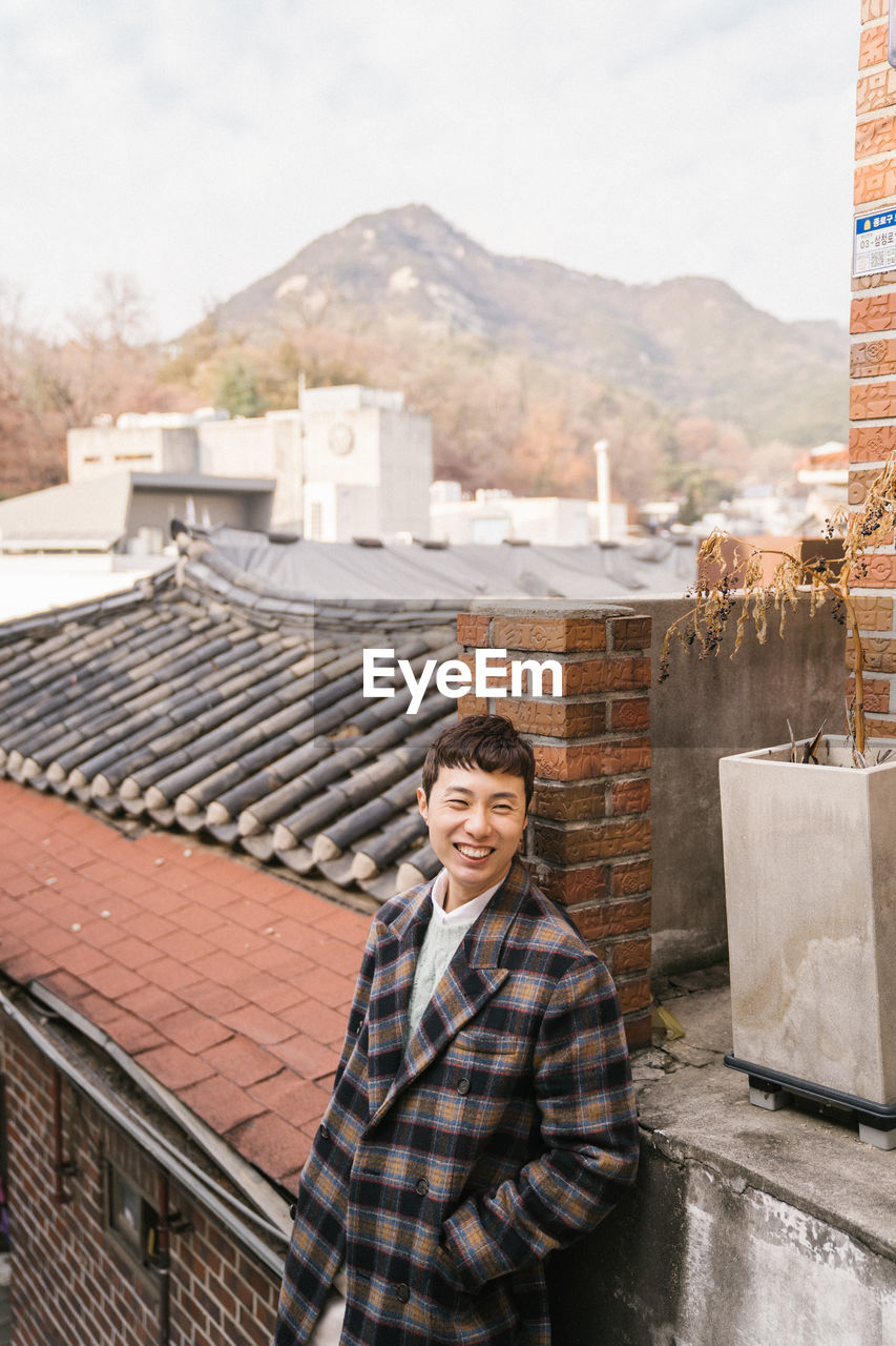 Portrait of smiling man standing by rooftop against sky