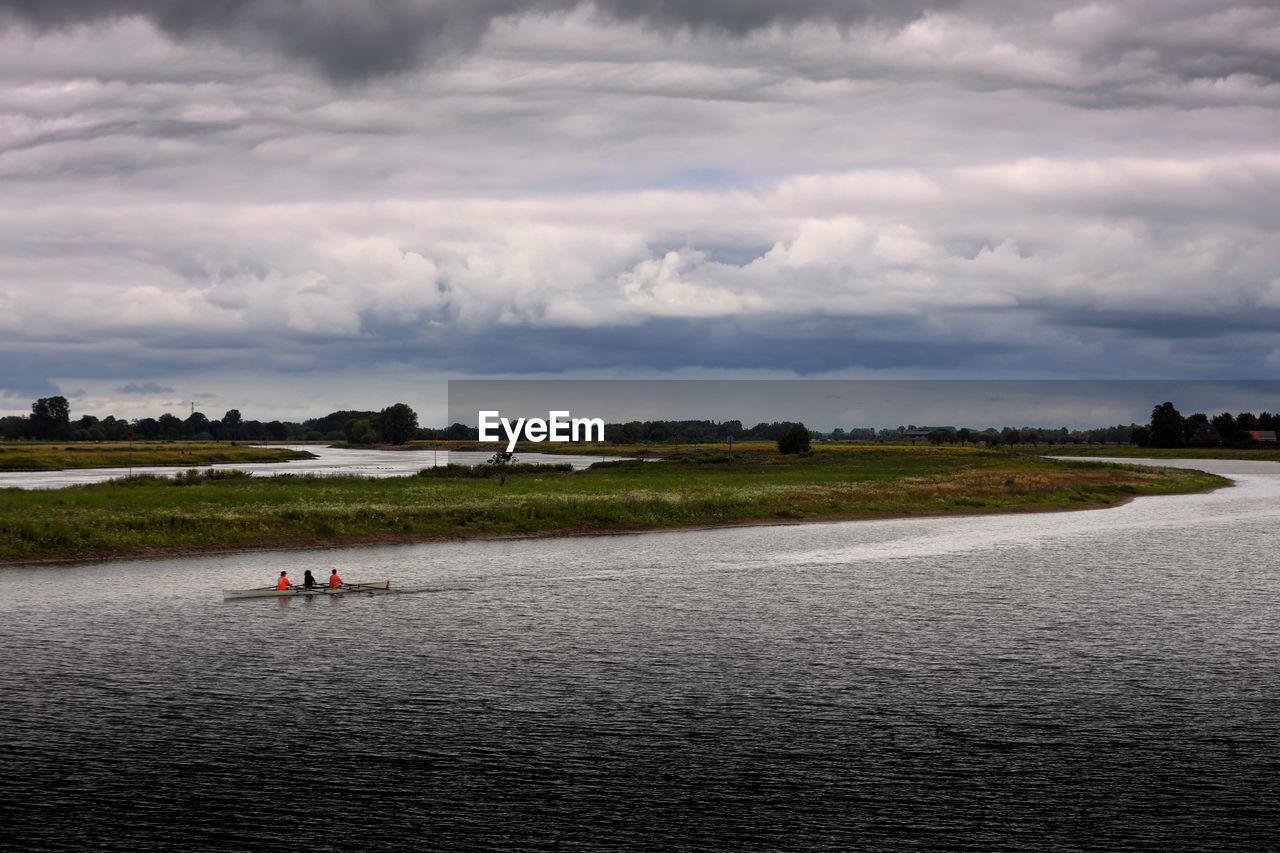 Friends rowing boat in lake against cloudy sky