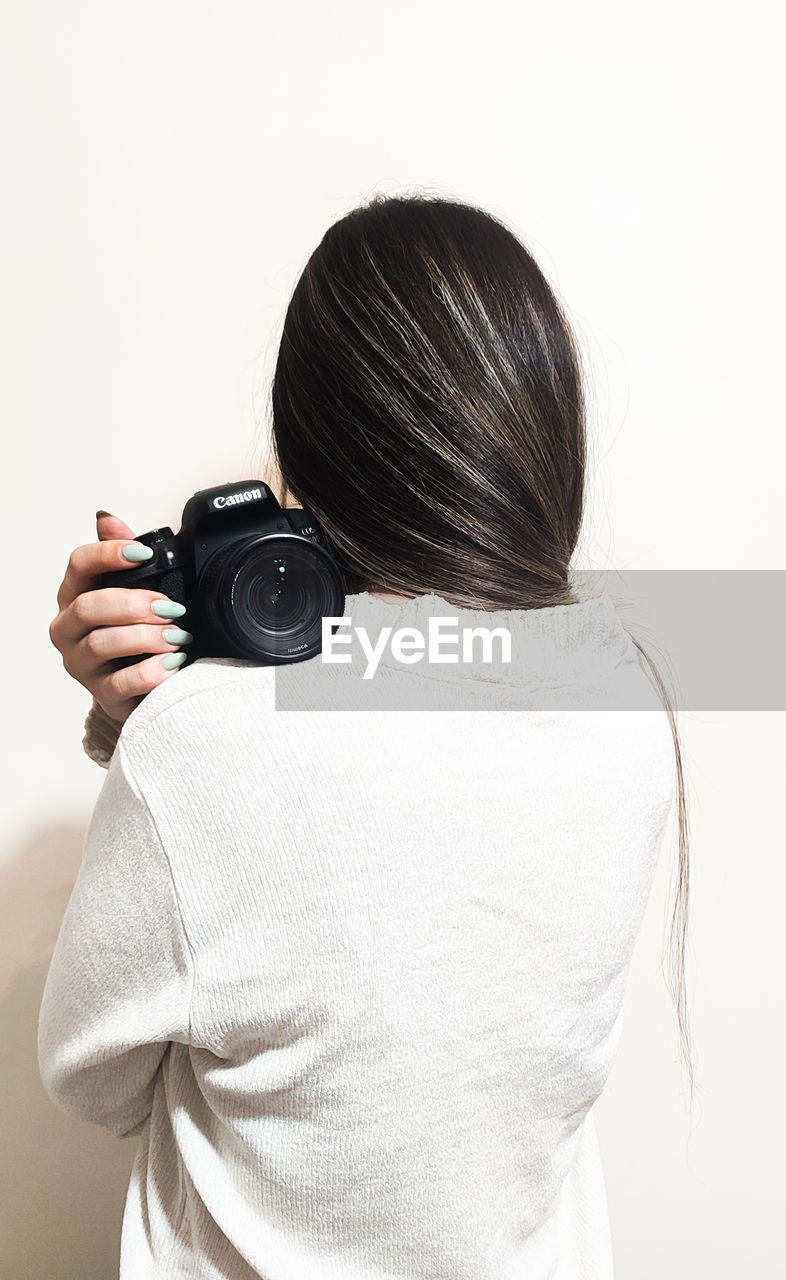 side view of woman photographing with camera against wall