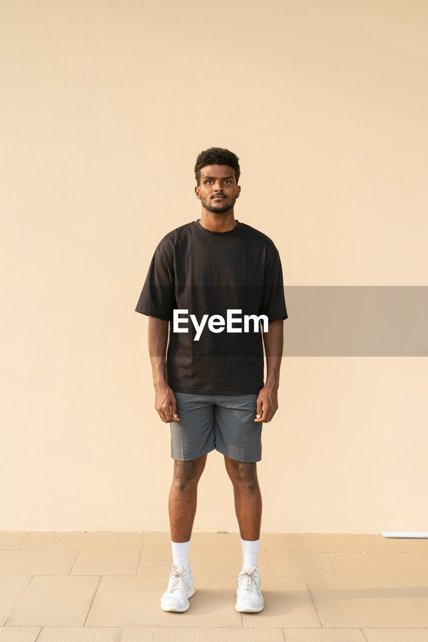 Portrait of handsome young african man wearing oversized black t-shirt full length shot