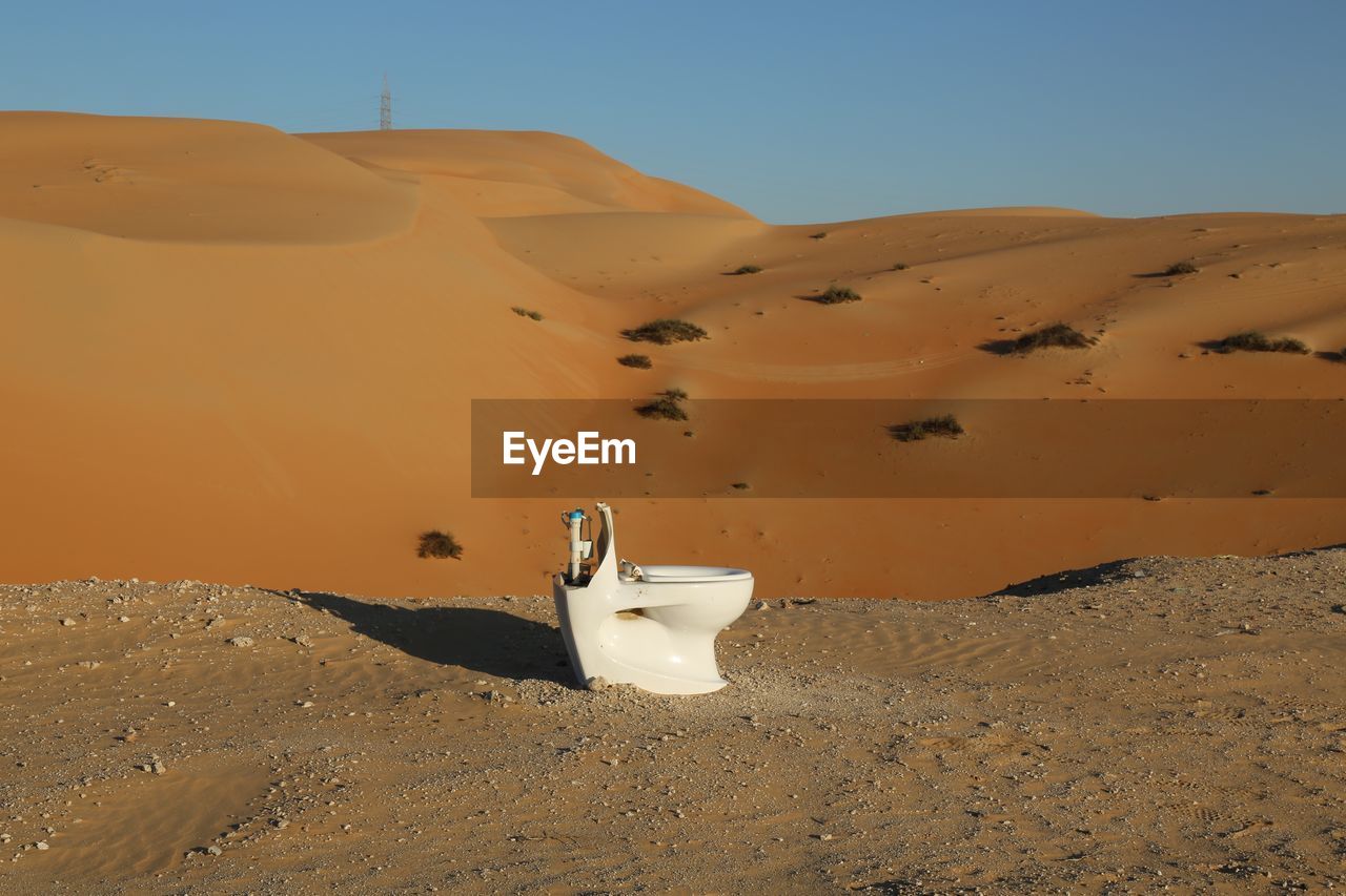 Toilet bowl on sand in desert against sky