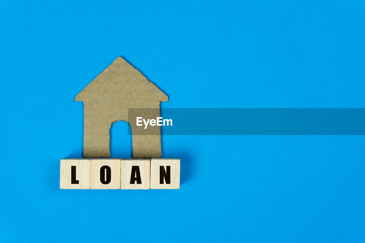 Home loan concept. a small house paper with wooden block and text on blue background and copy space.