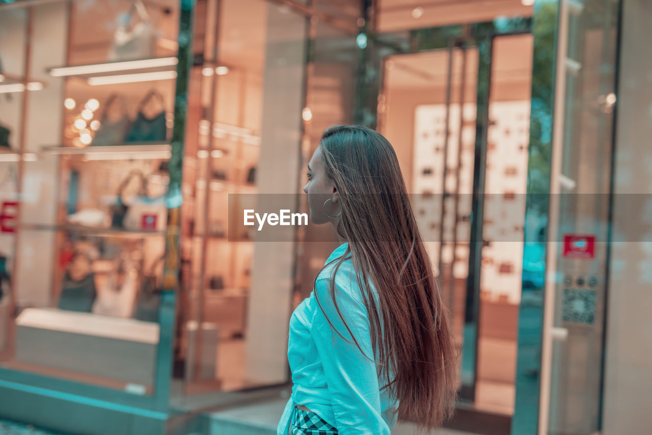 Side view of woman standing on footpath by store window