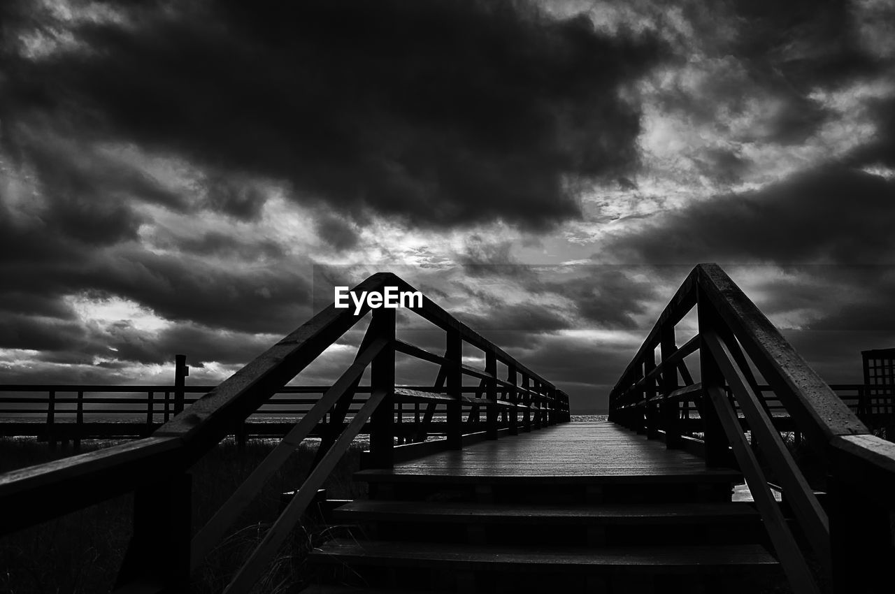 Bridge over calm sea against cloudy sky