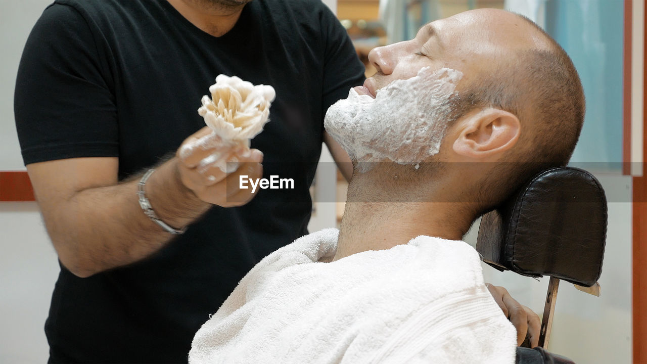 Barber applying shaving cream on mature man in salon