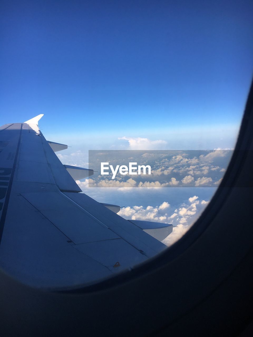 Cropped image of airplane flying against clear blue sky seen through window