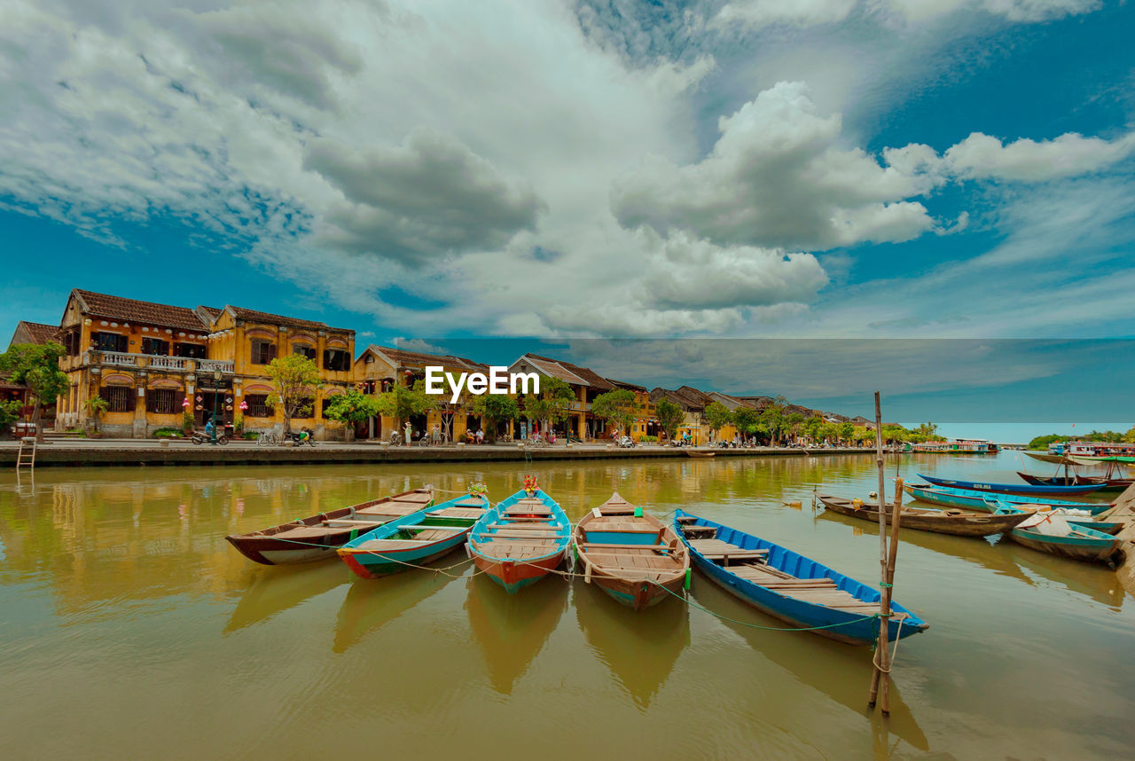 Boats moored in lake against cloudy sky