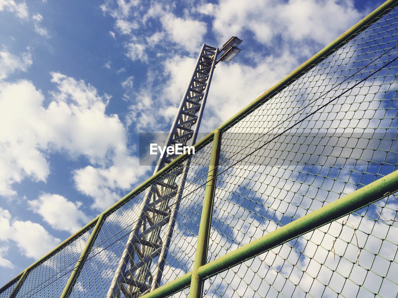Low angle view of floodlight and chainlink fence against sky