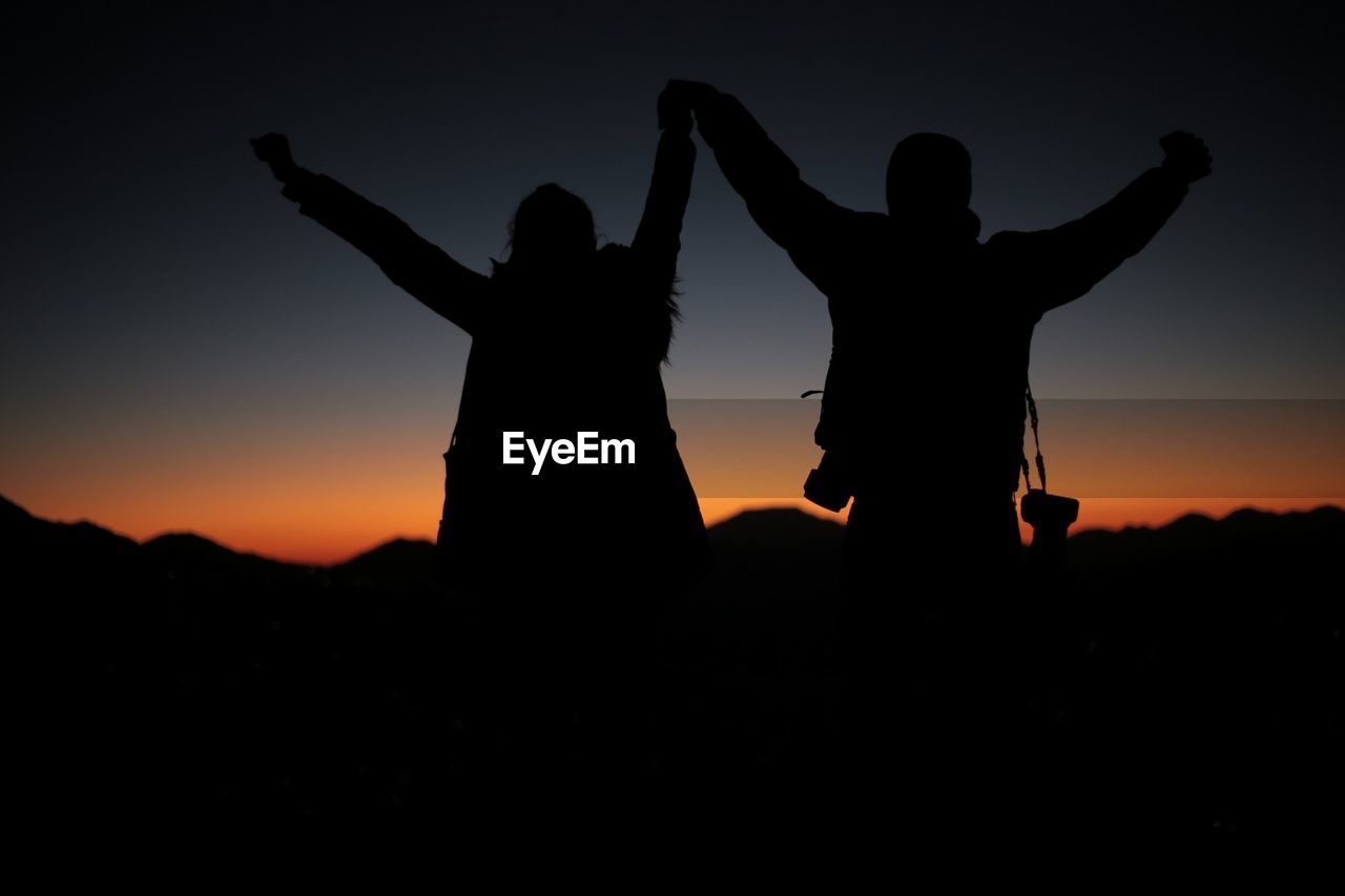 Silhouette people with arms raised against sky during sunset