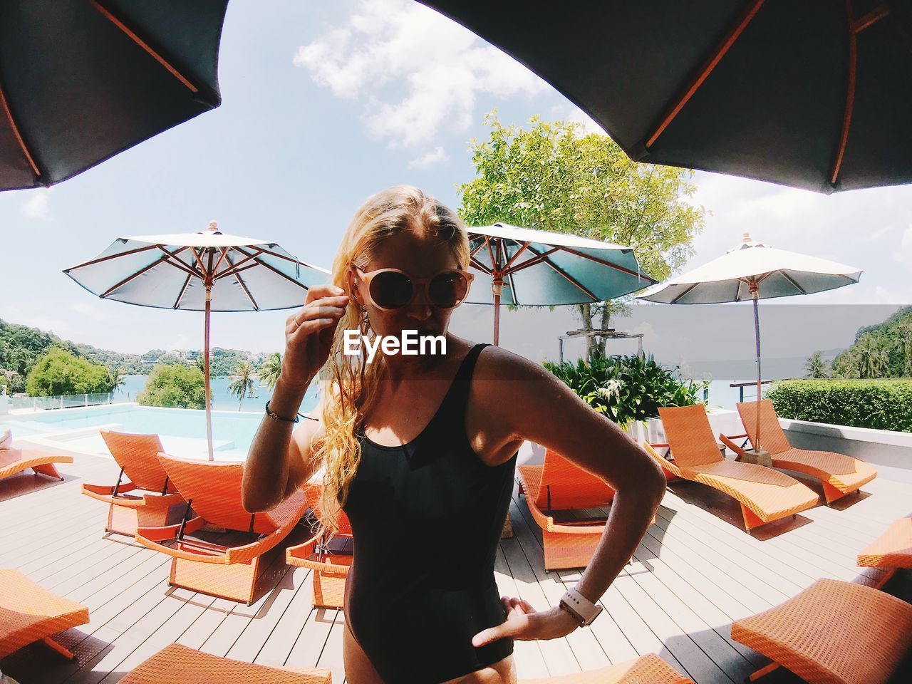 Portrait of woman wearing sunglasses amidst lounge chair at poolside