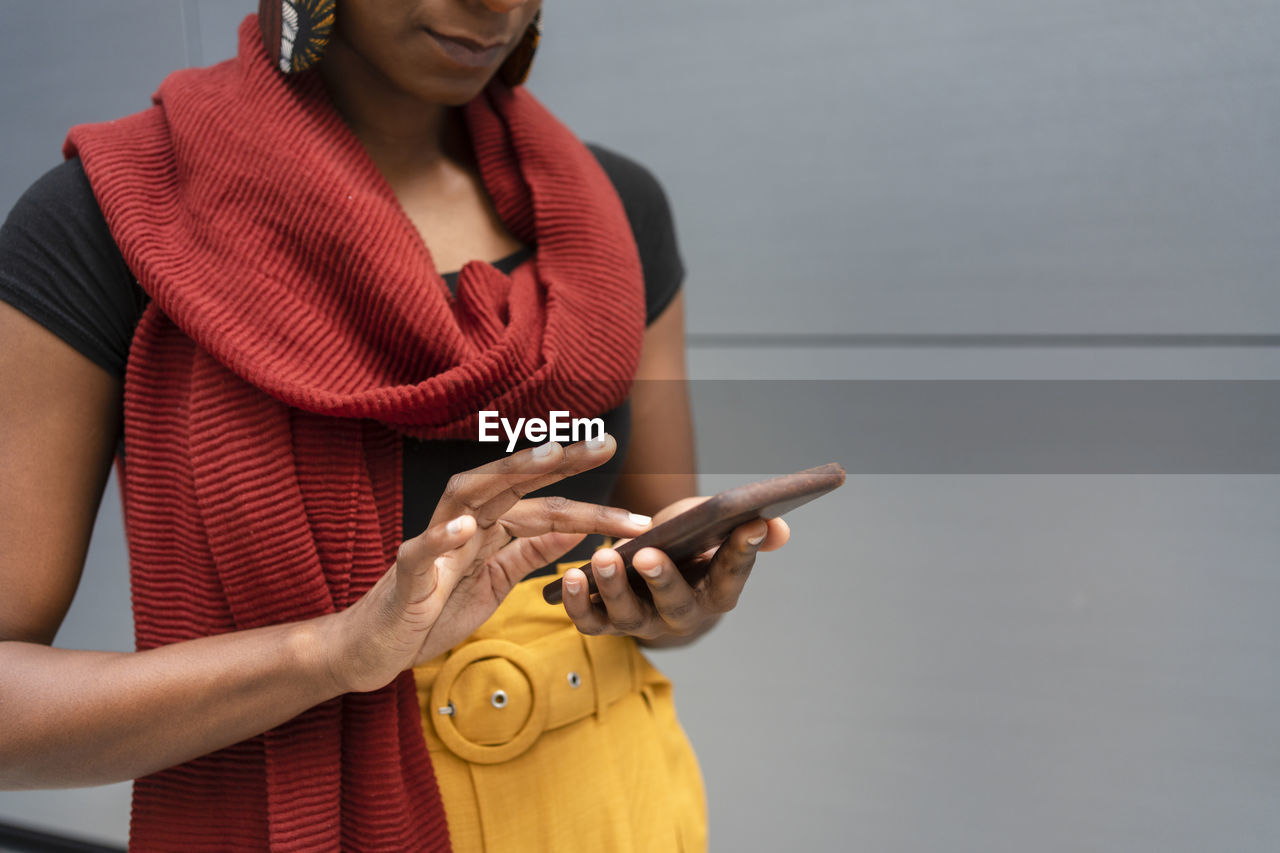 Woman wearing scarf using smart phone in front of gray wall