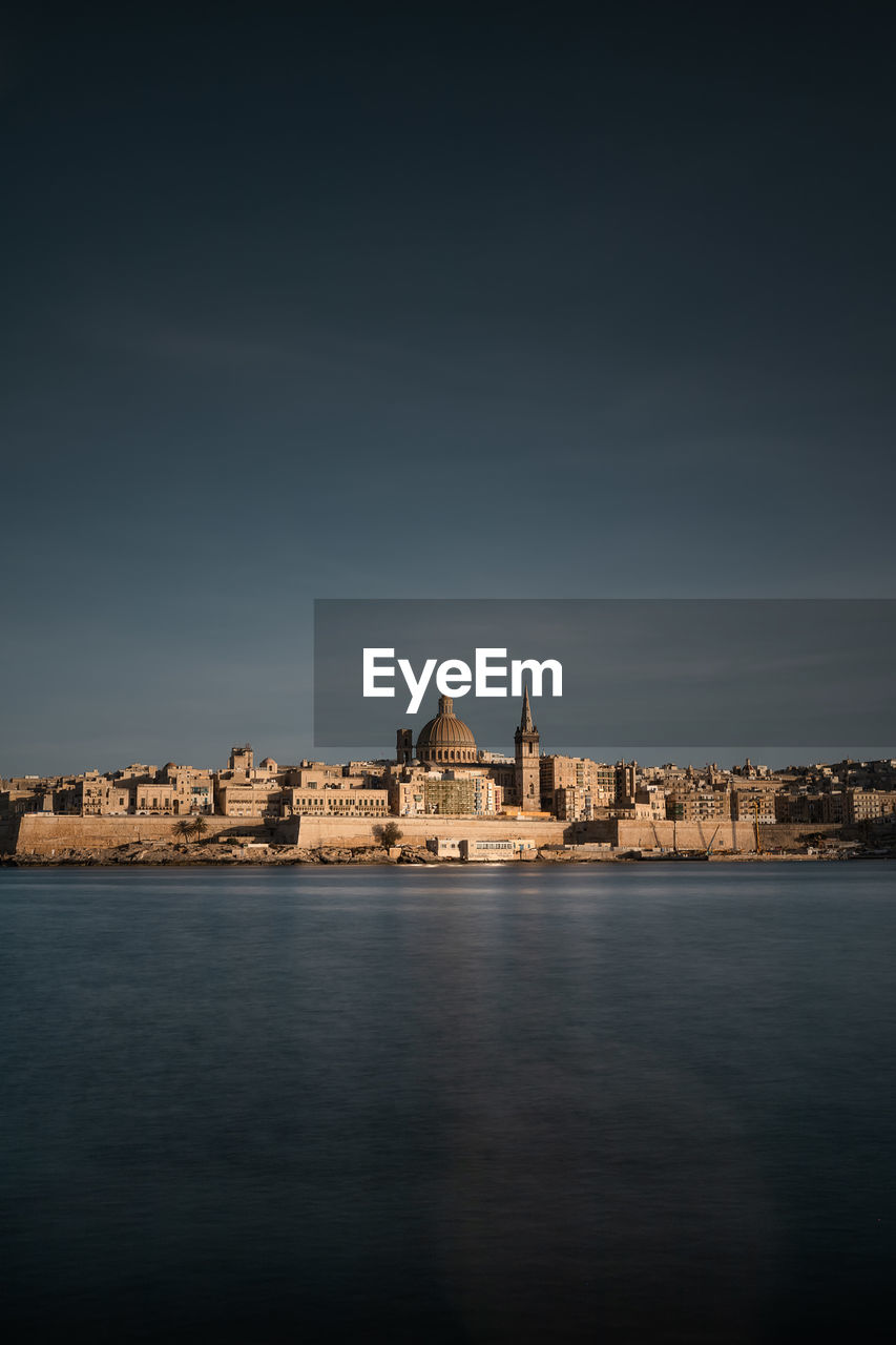 View of buildings by sea against sky in city