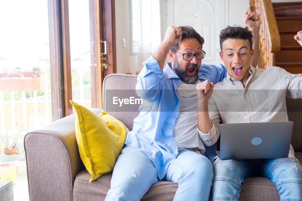 Cheerful father and son celebrating while using laptop