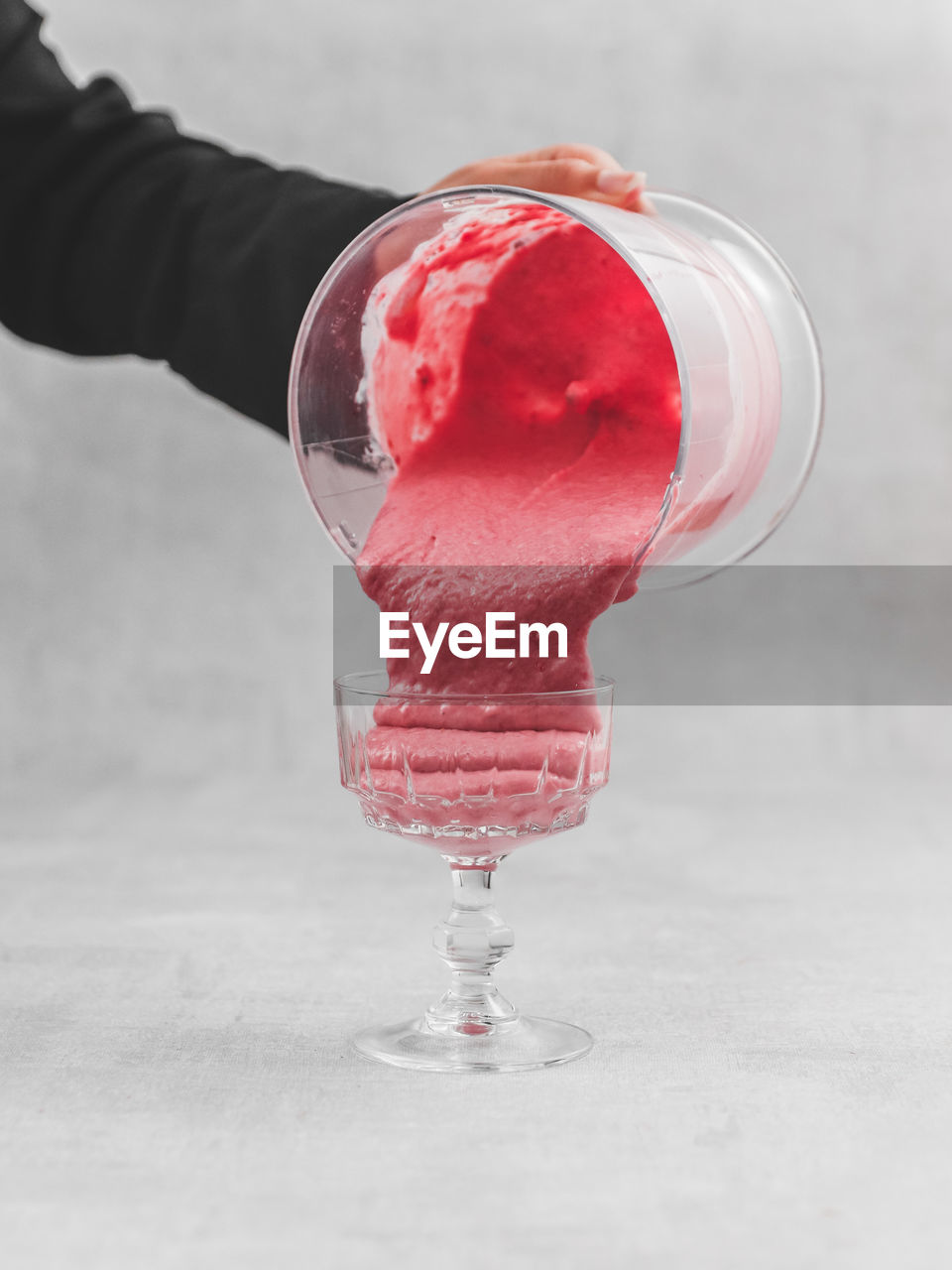 Midsection of person pouring pink raspberry mousse in crystal glass
