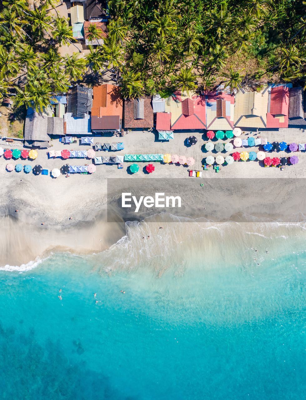Aerial view of a jungle lined beach. colorful roofs and umbrellas line the vibrant beach in bali