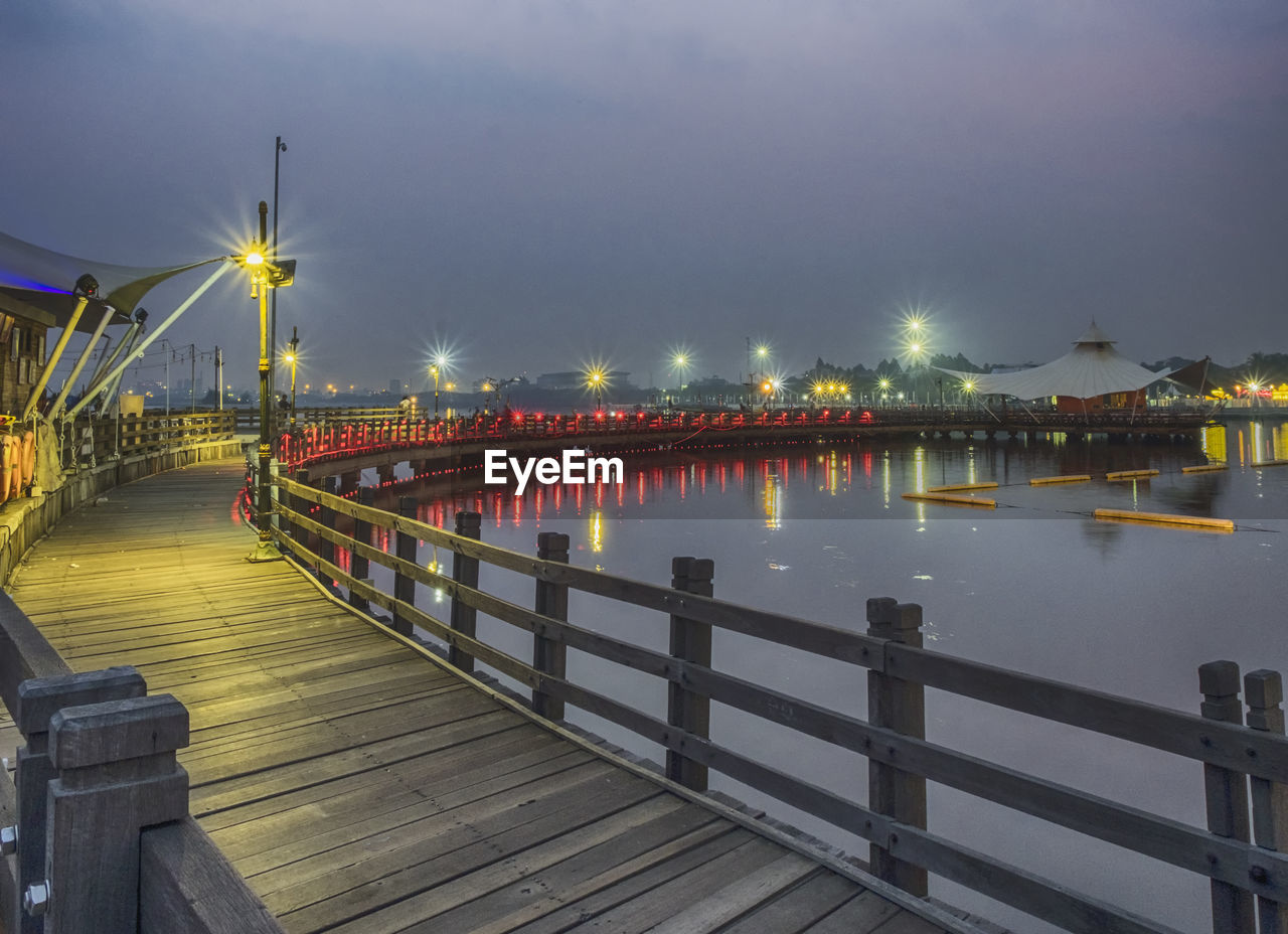 Illuminated footbridge over lake against sky during night