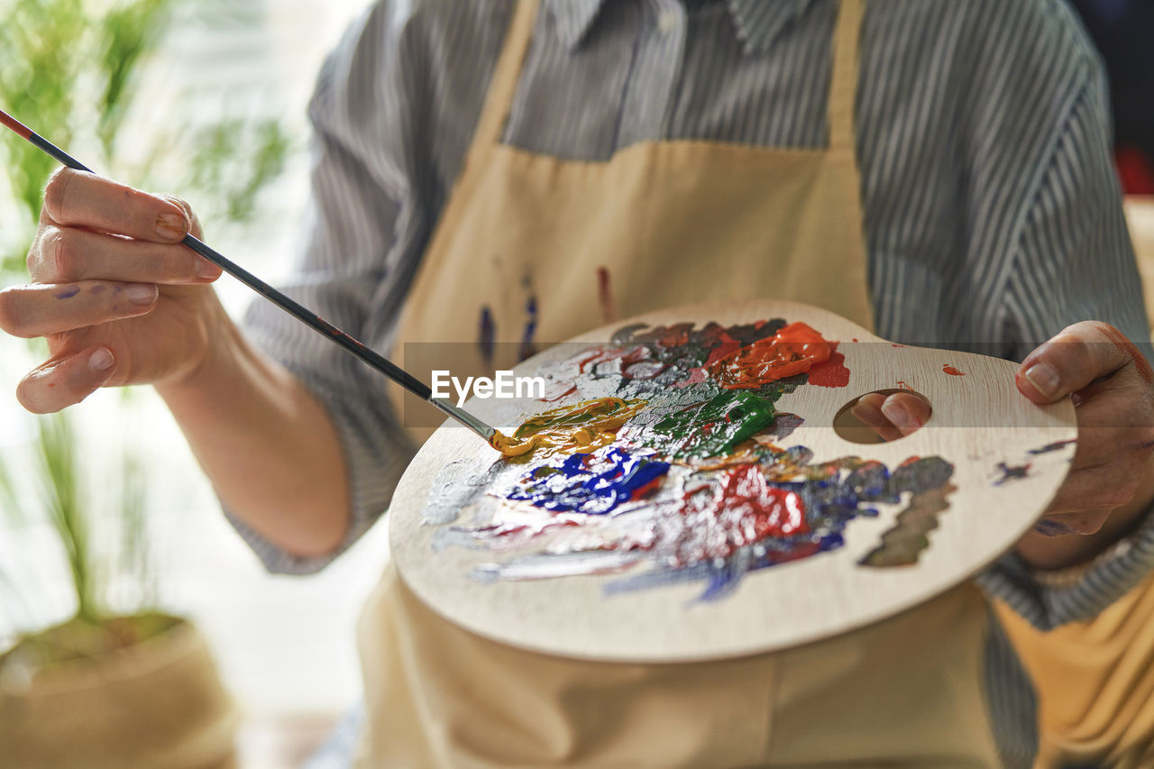 Woman holding palette while mixing colors through paintbrush at home