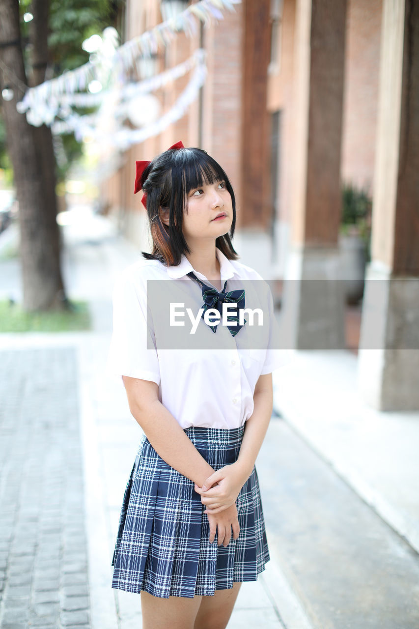 Young woman looking away while standing outdoors