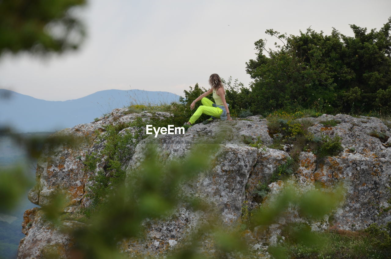 Wife sitting on rock against mountain