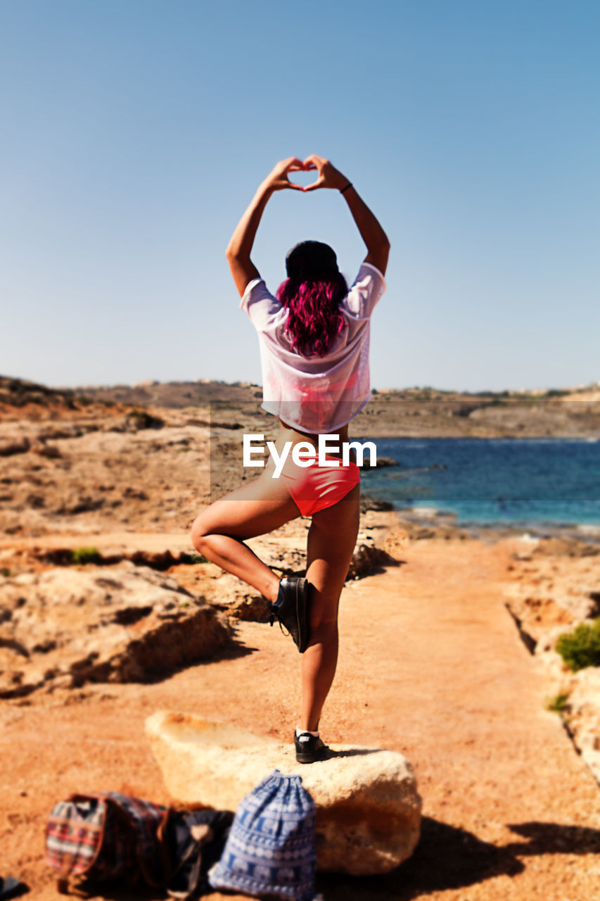 Rear view of young woman posing on rock against clear sky