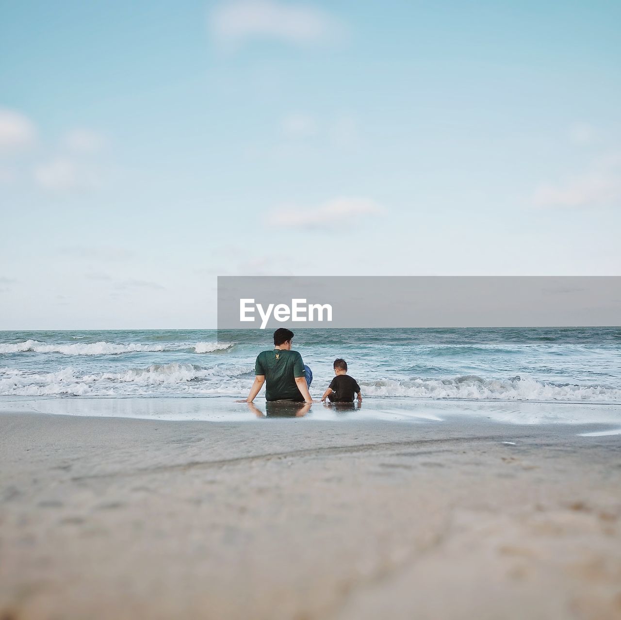 Surface level view of father and son sitting at beach against sky