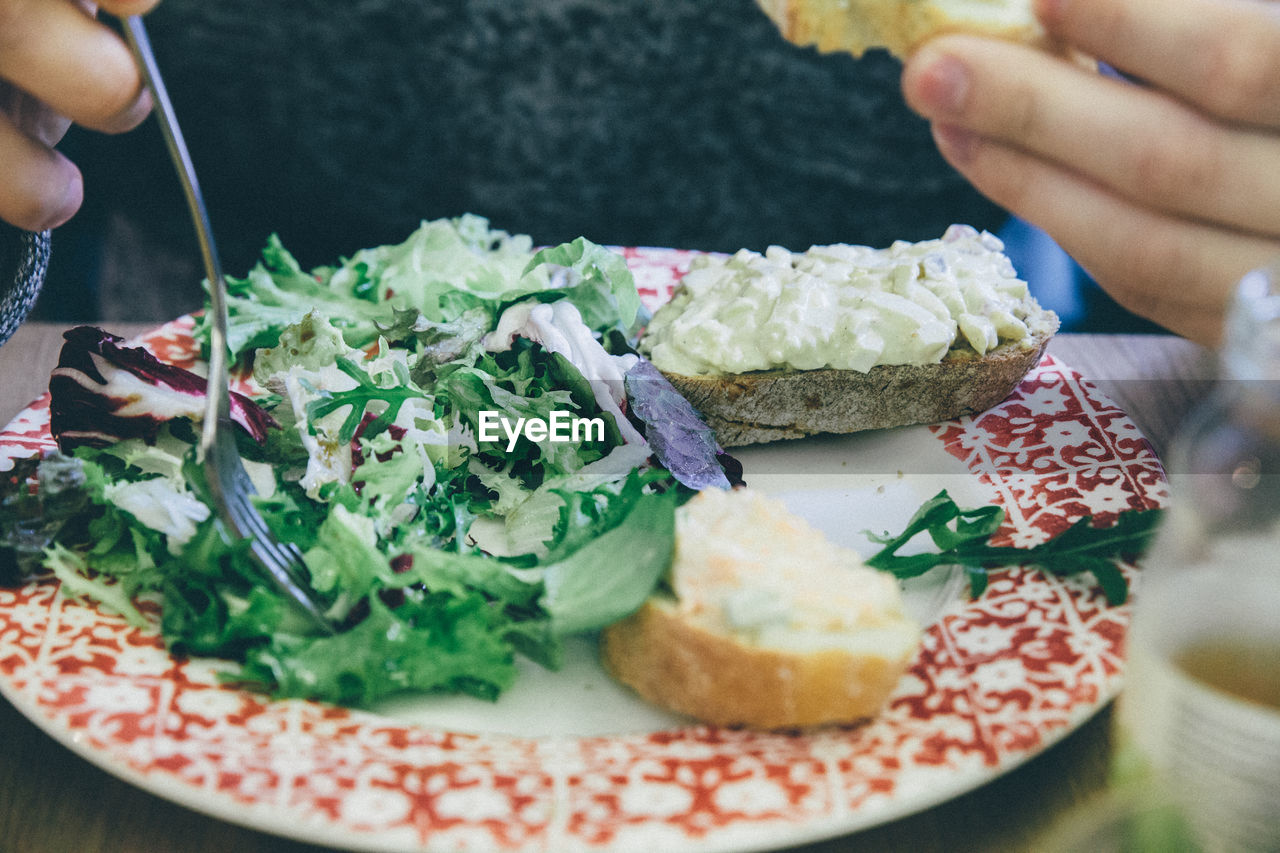 Midsection of person holding fork over salad