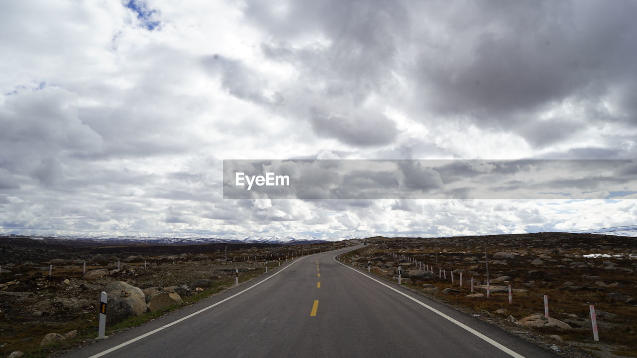 Empty road amidst landscape against cloudy sky