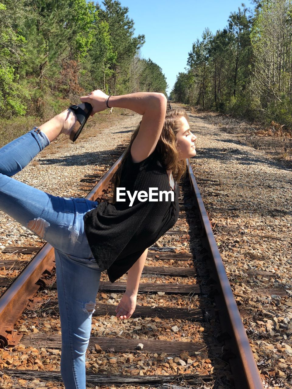 SIDE VIEW OF YOUNG WOMAN STANDING ON RAILROAD TRACK