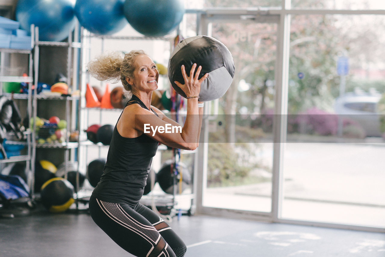 Portrait of smiling woman exercising with medicine ball while at gym