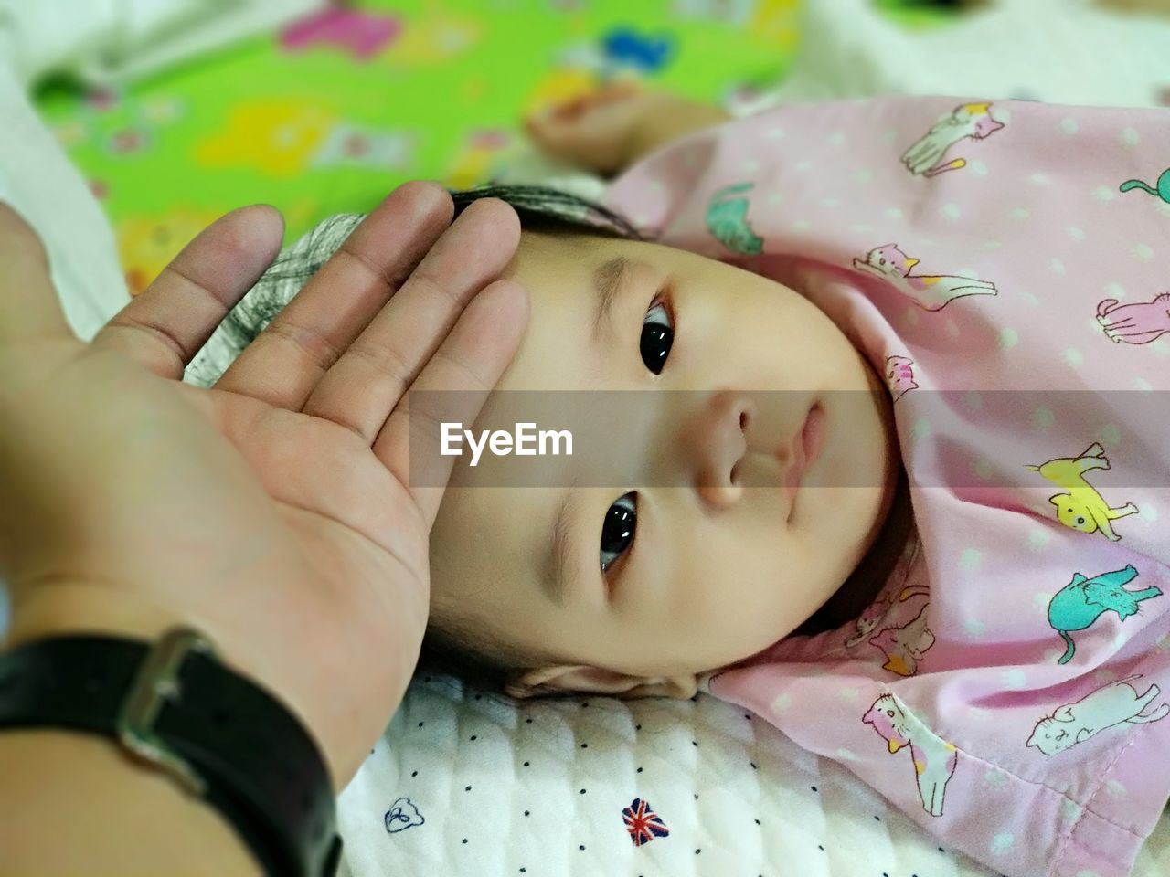 Cropped hand of person touching baby girl forehead at home