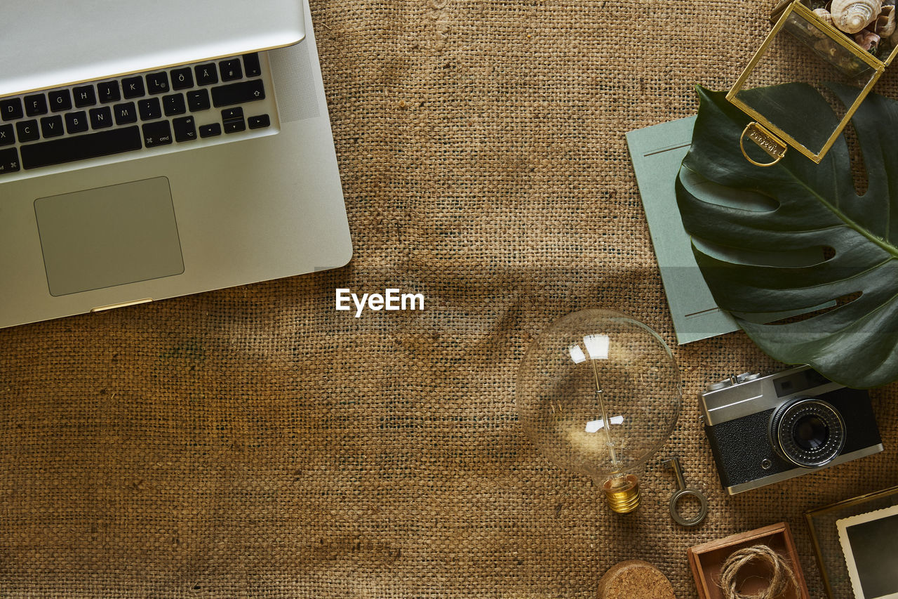 High angle view of light bulb with laptop and camera on burlap