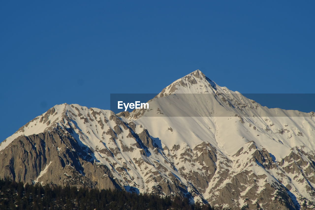 Low angle view of snowcapped mountains against clear blue sky