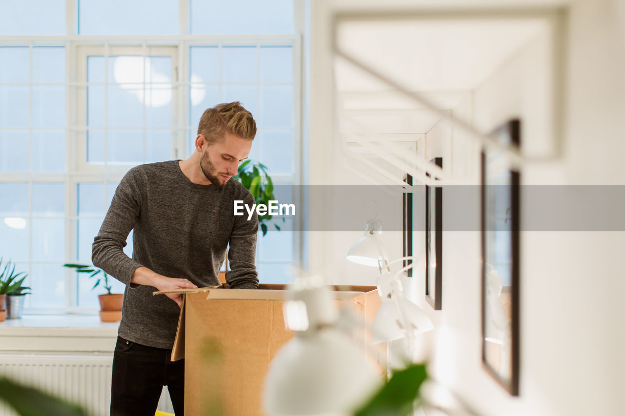 Young businessman opening cardboard box at illuminated creative office