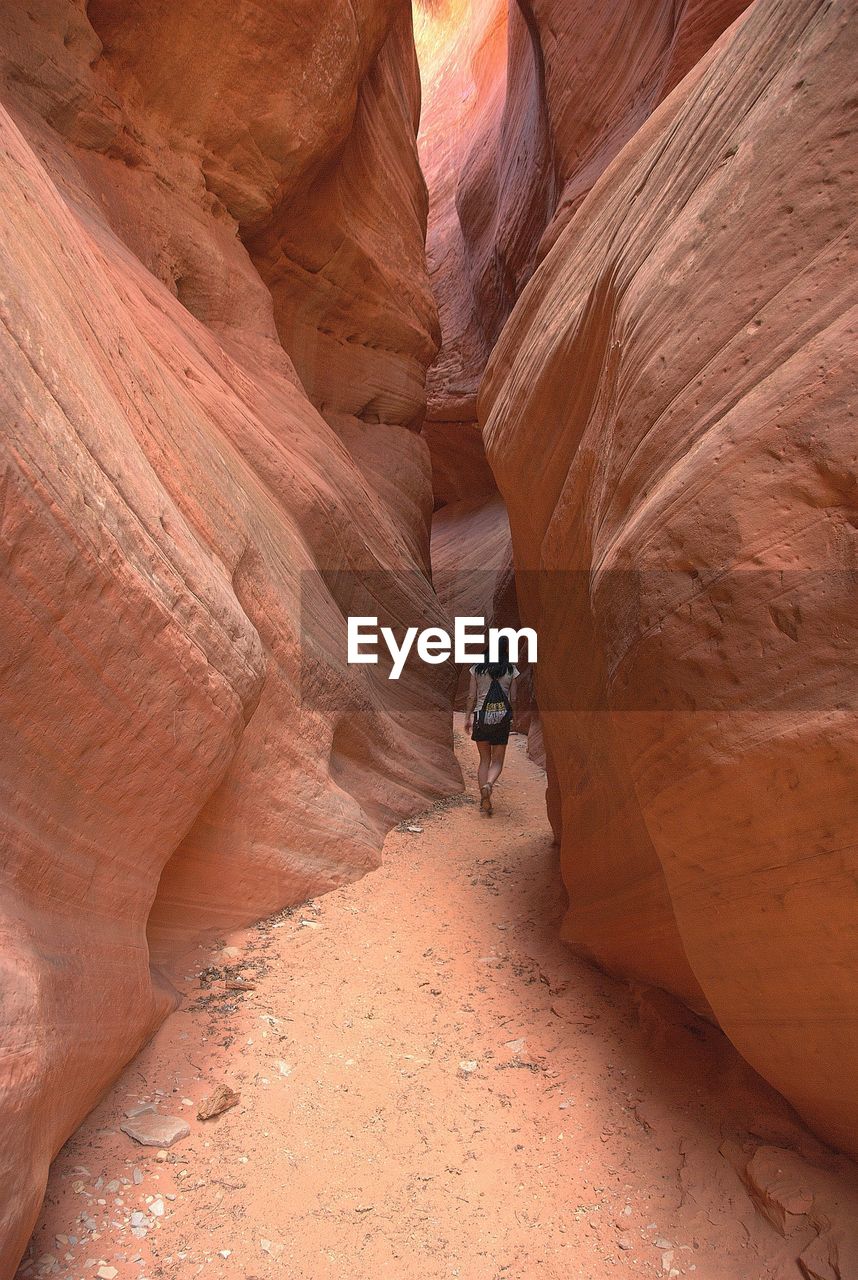 Rear view of woman walking amidst rock formation at slot canyon