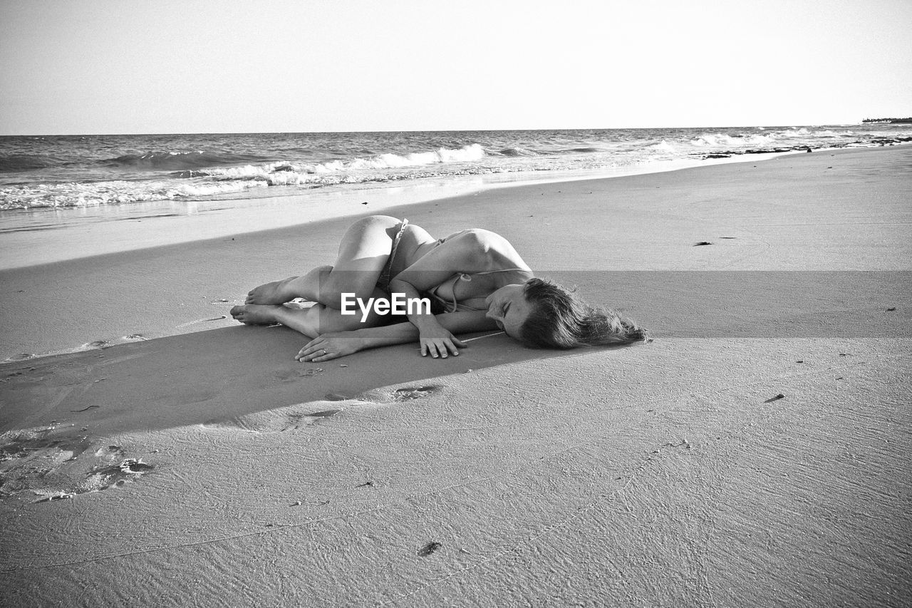 Young woman lying on sand at beach against clear sky