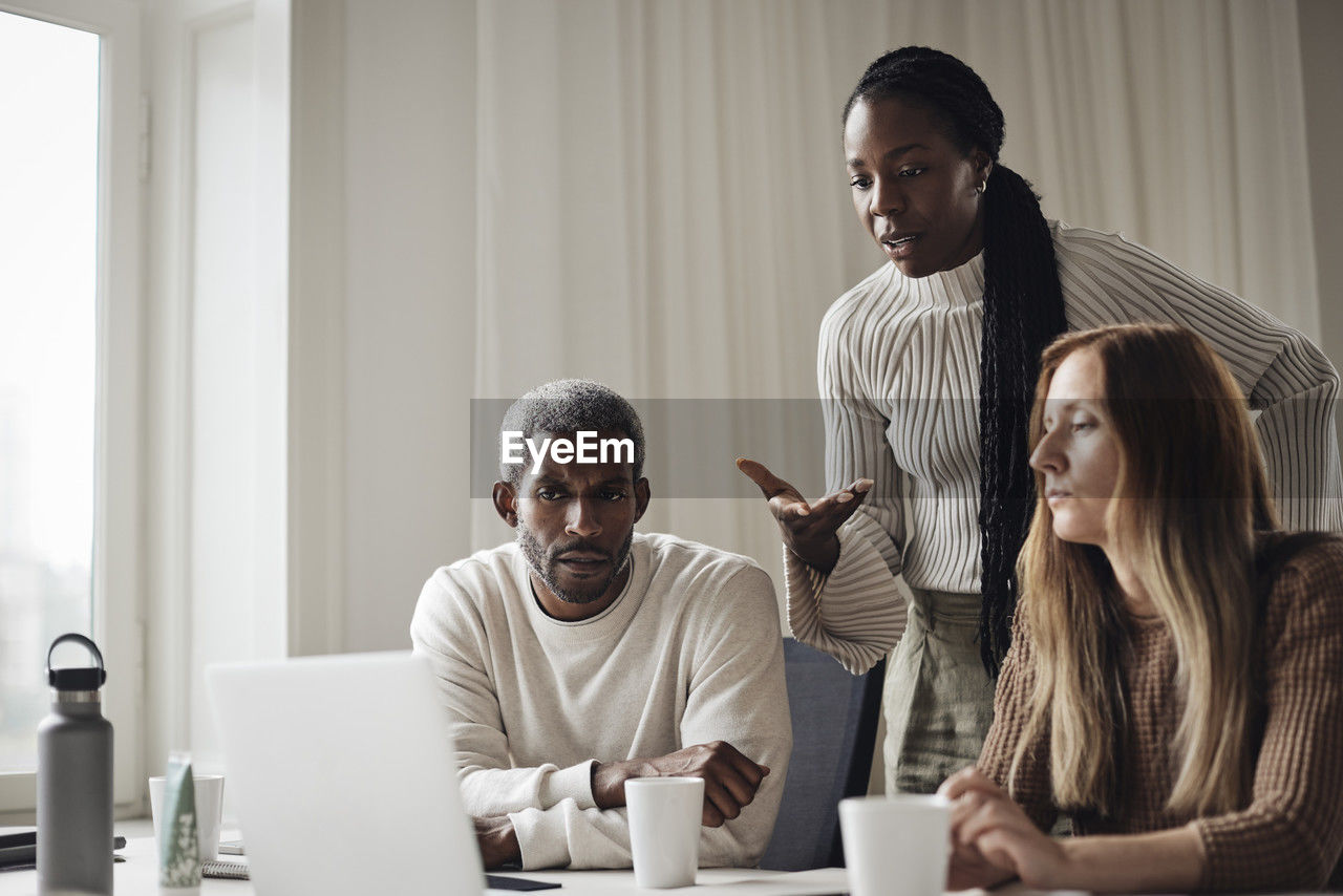 Businesswoman explaining colleagues while looking at laptop in office