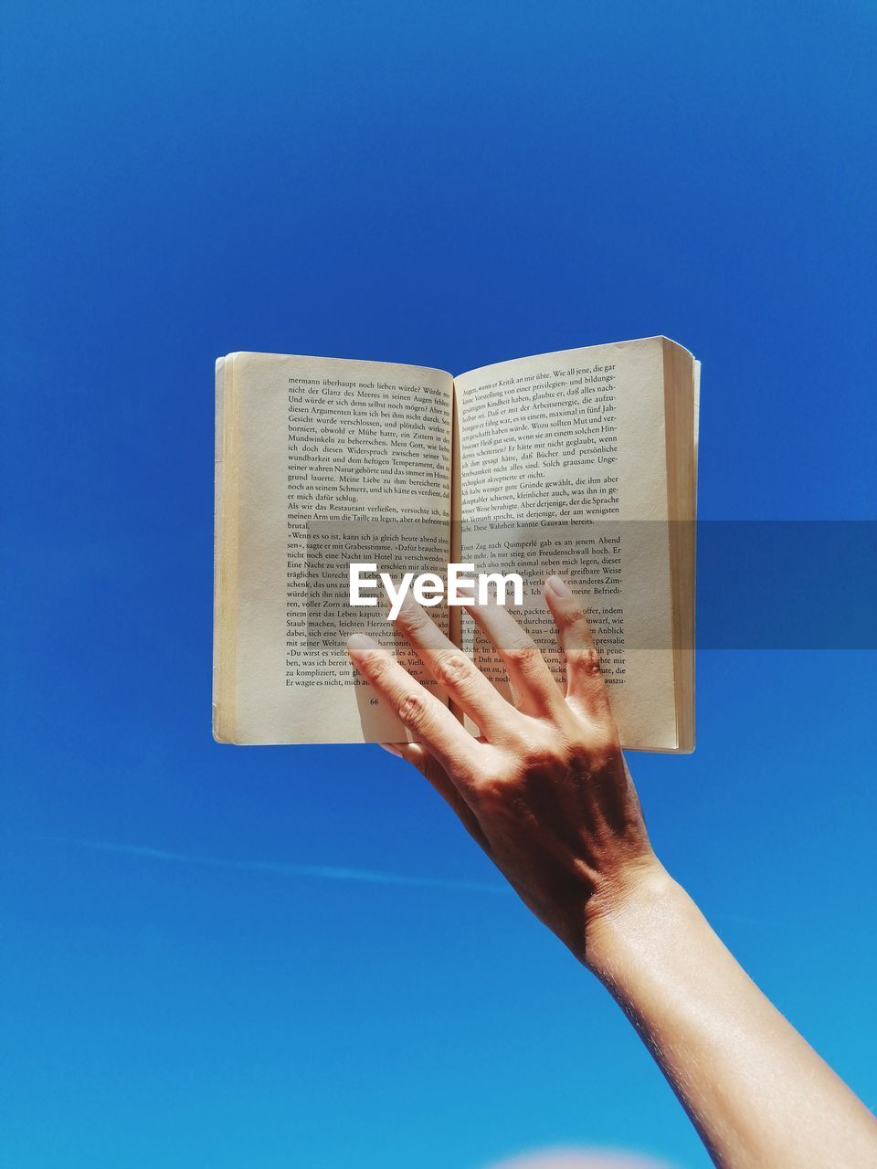 Cropped hand of person holding book against blue background