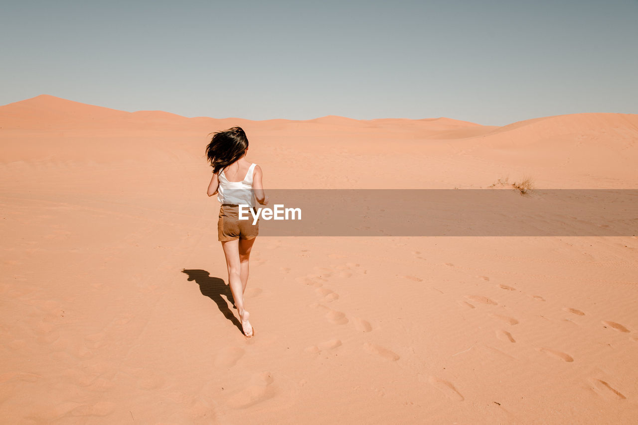 Young woman running through the sand dunes in the desert of the sahara