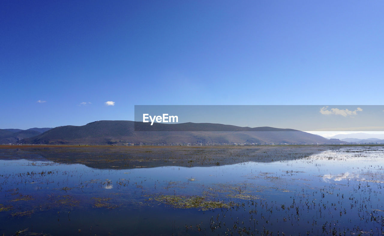 SCENIC VIEW OF LAKE BY MOUNTAINS AGAINST BLUE SKY