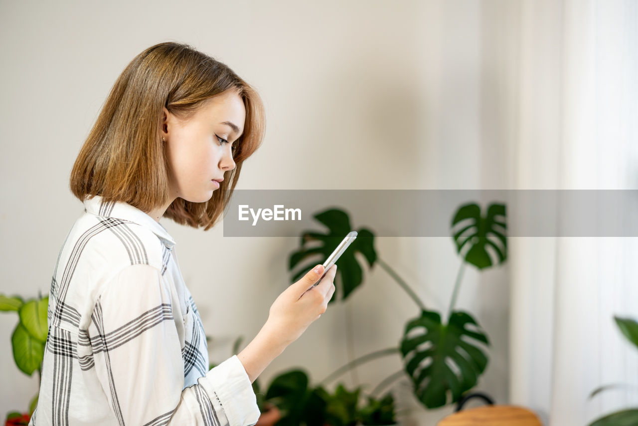 Young woman holding smartphone using mobile apps, chatting in social media at home.