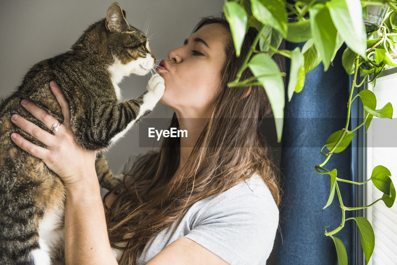 Woman indoors at home kissing her cat by the window