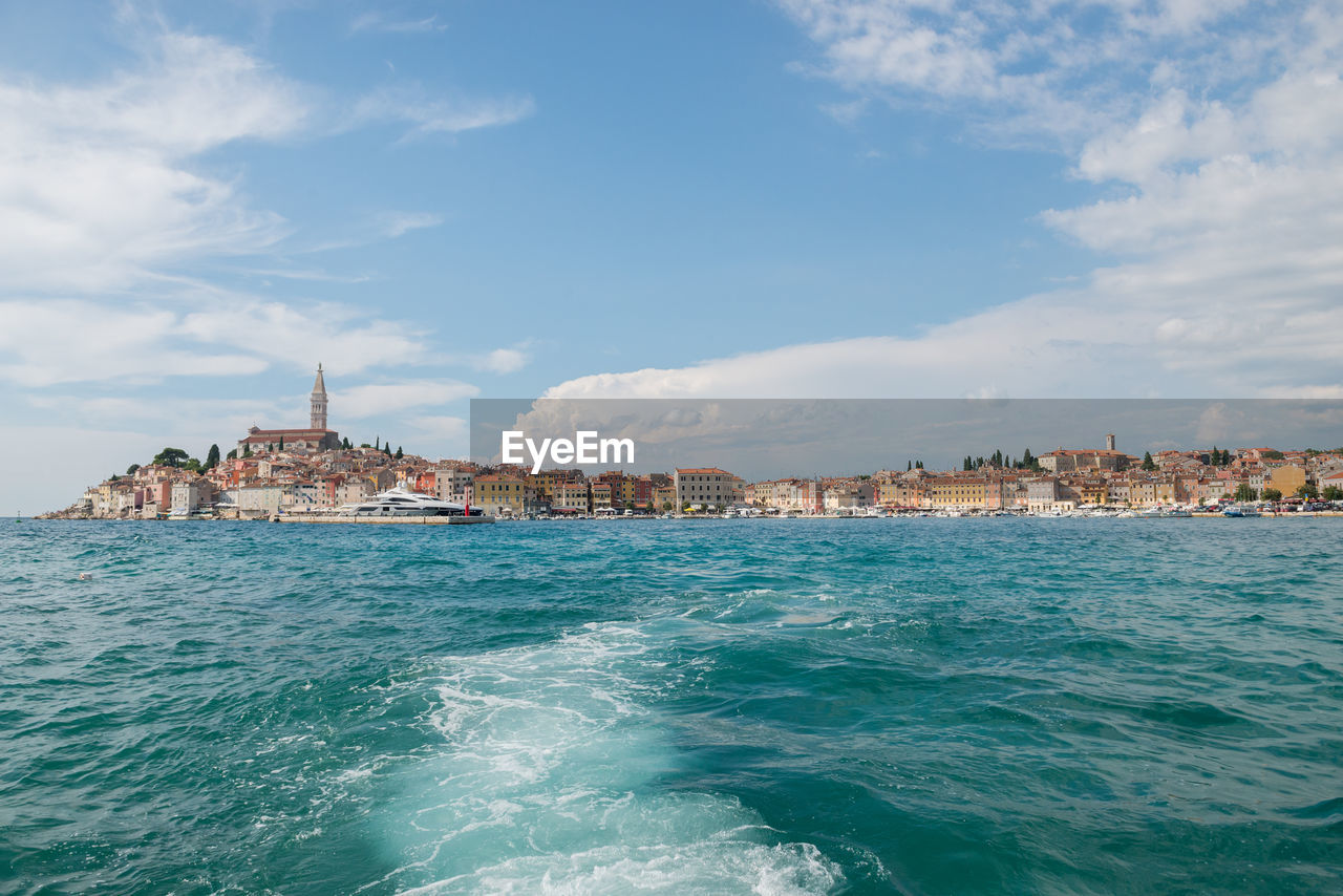 View of buildings by sea against cloudy sky