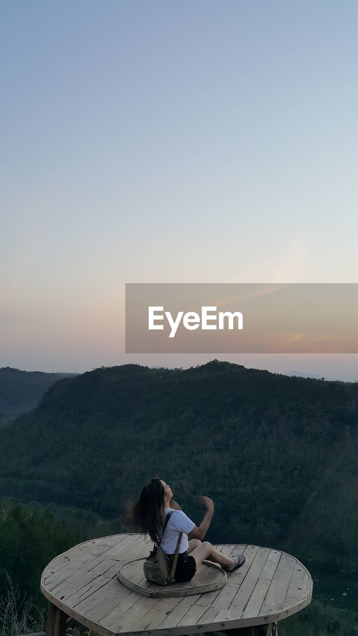 Woman sitting on wood against clear sky