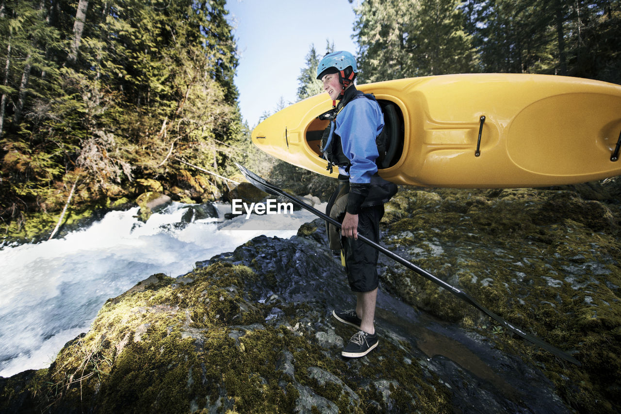 Man carrying kayak while standing by river in forest