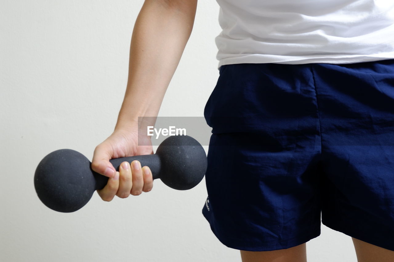 Midsection of man holding dumbbell while standing against wall