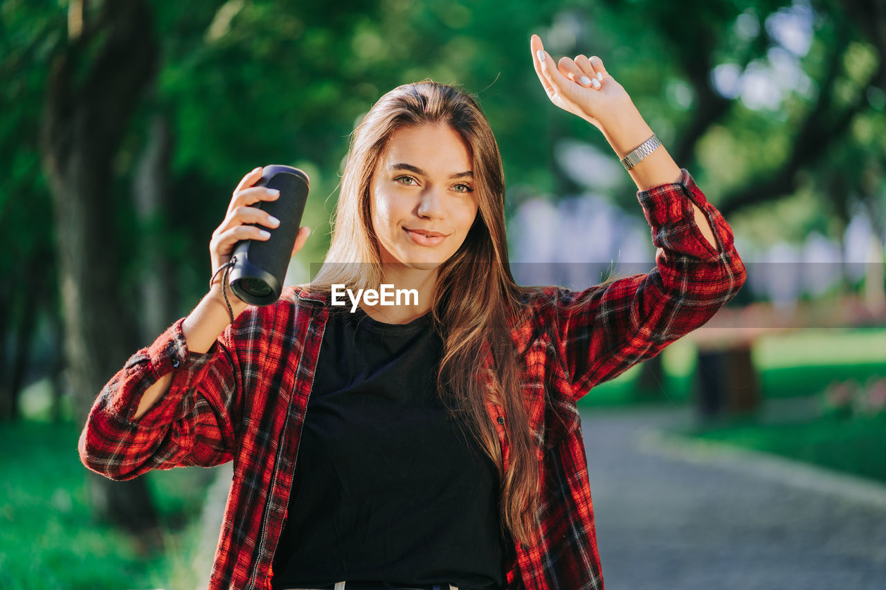 Smiling young woman holding speaker enjoying music at park